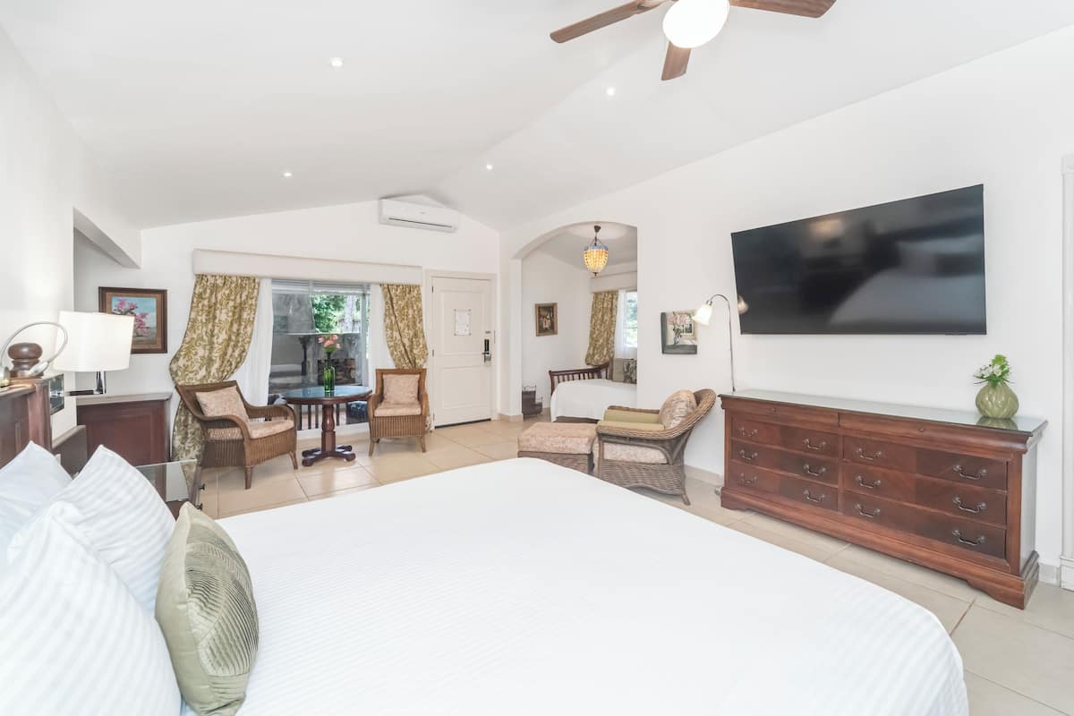 A spacious bedroom with a large bed, a wooden dresser, a flat-screen TV, and a dining area with wicker furniture.