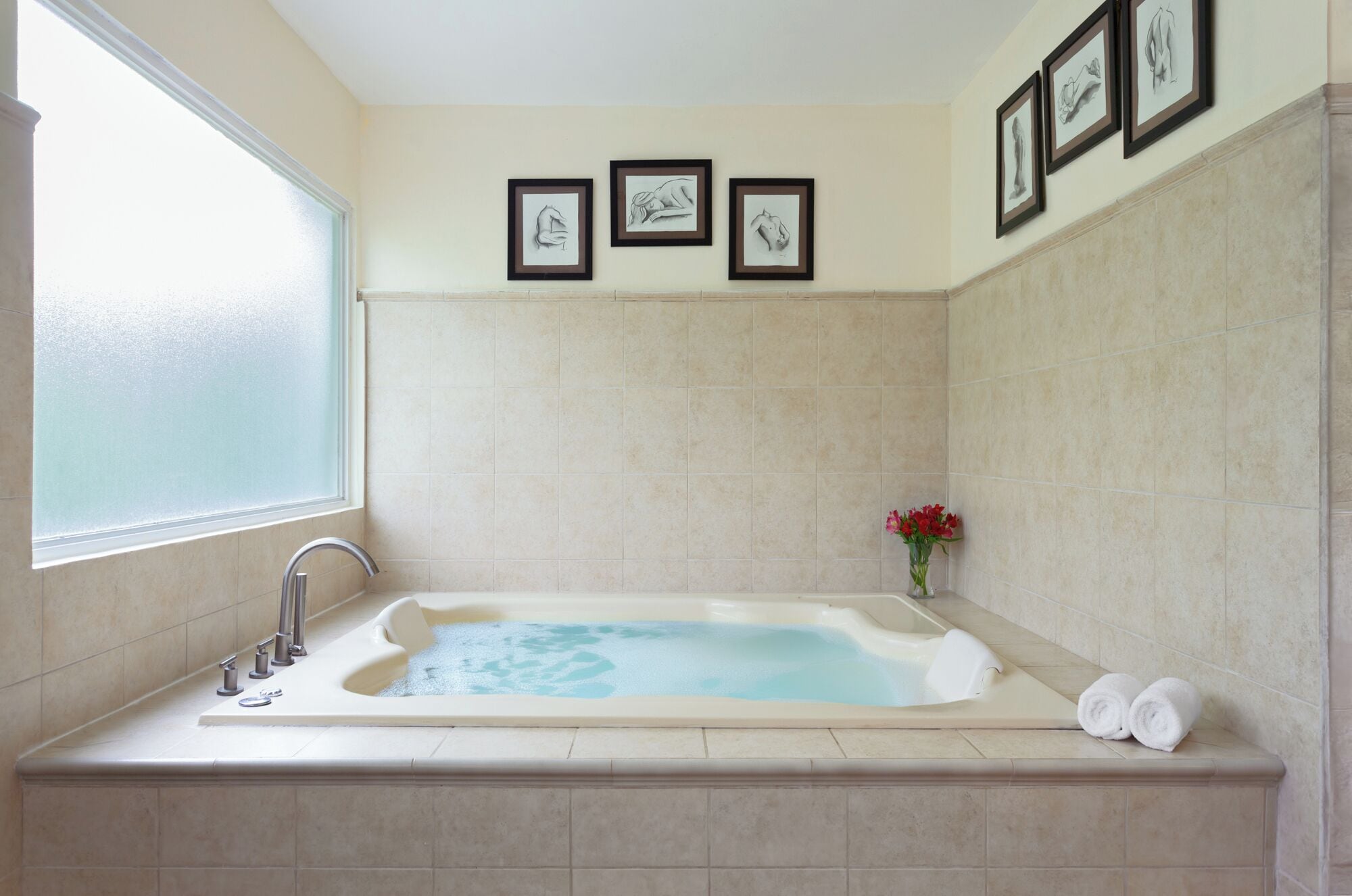 A bathroom with a large bathtub, a window, and three framed pictures on the wall.