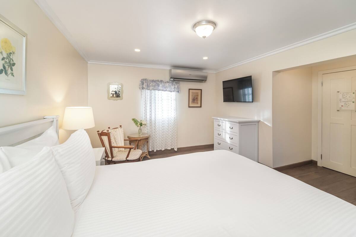 A hotel room with a large bed, a desk, a chair, a TV, and a wardrobe.
