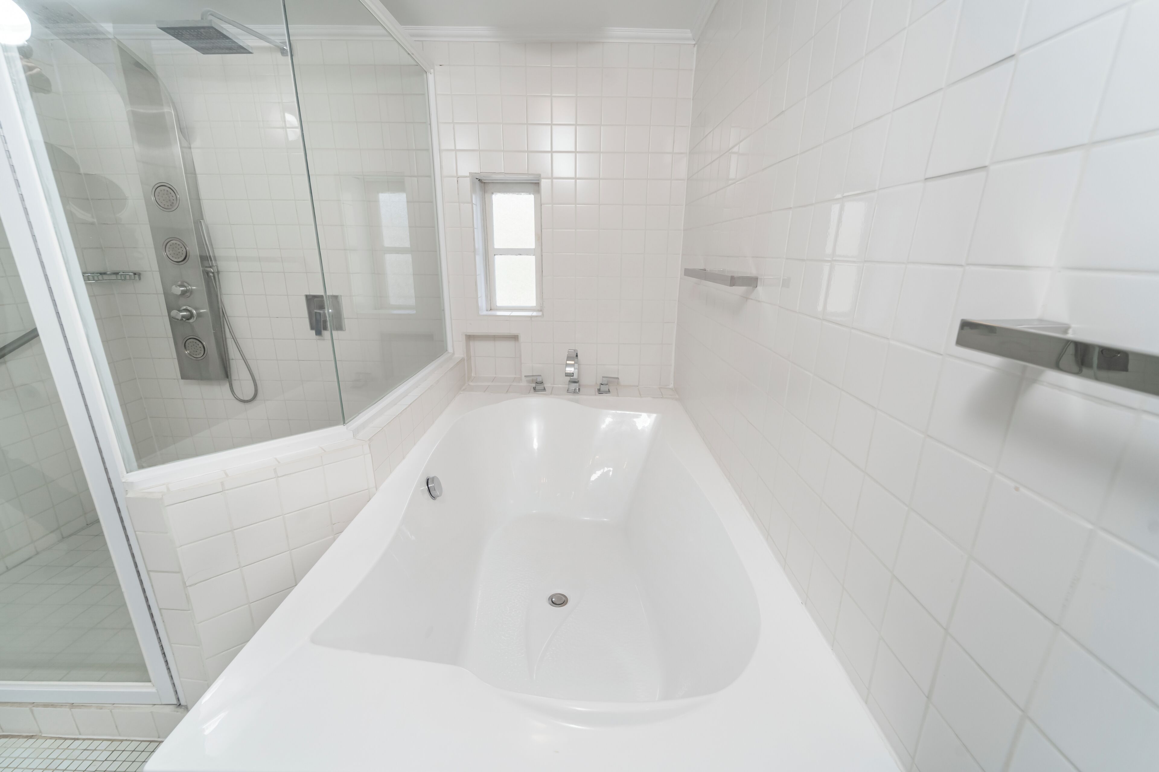Un baño moderno con ducha de vidrio, una bañera grande y paredes de azulejos blancos.
