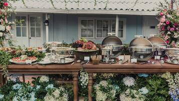 A buffet table with various dishes and drinks, set up outdoors with a house in the background.