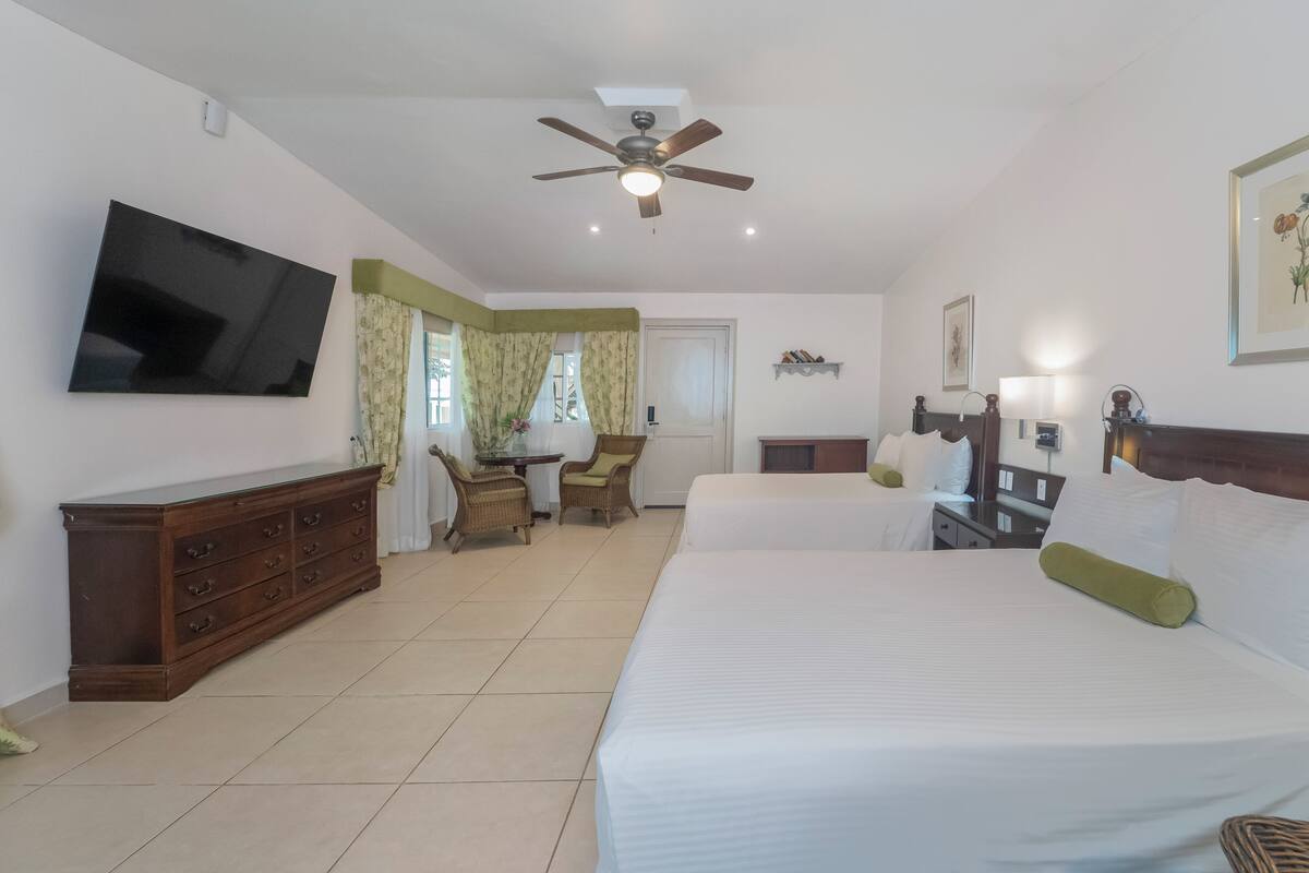 A hotel room with a bed, a TV, a ceiling fan, a dresser, a chair, and a small table.
