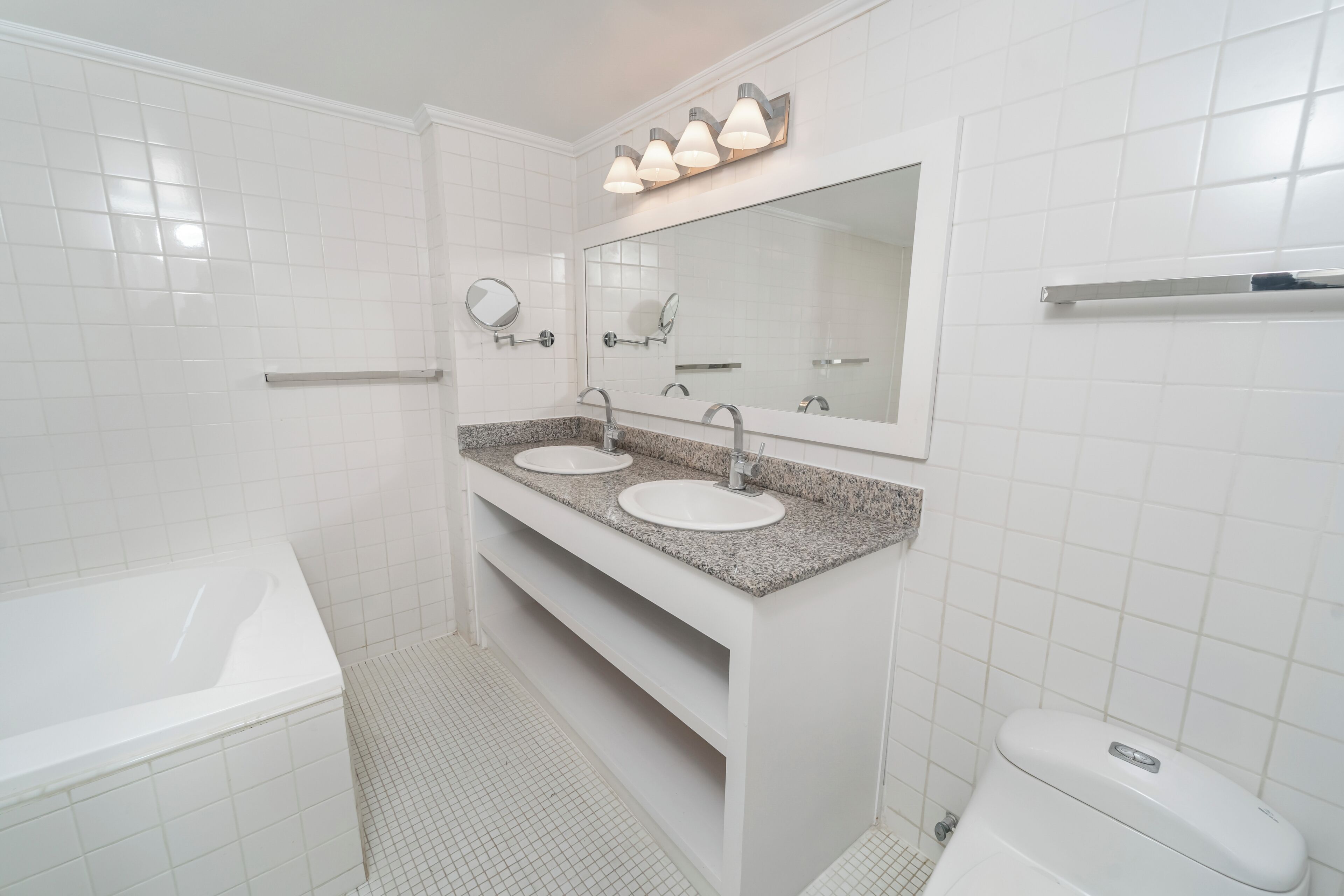 Een moderne badkamer met witte tegels, een dubbele wastafel, een grote spiegel en een bad.