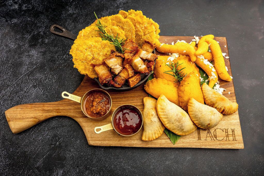 Tábua de madeira com plantains fritos, carne e empadas, acompanhada de acompanhamentos.