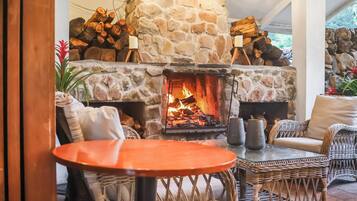 A stone fireplace with logs, wicker furniture, and a table in a cozy indoor setting.