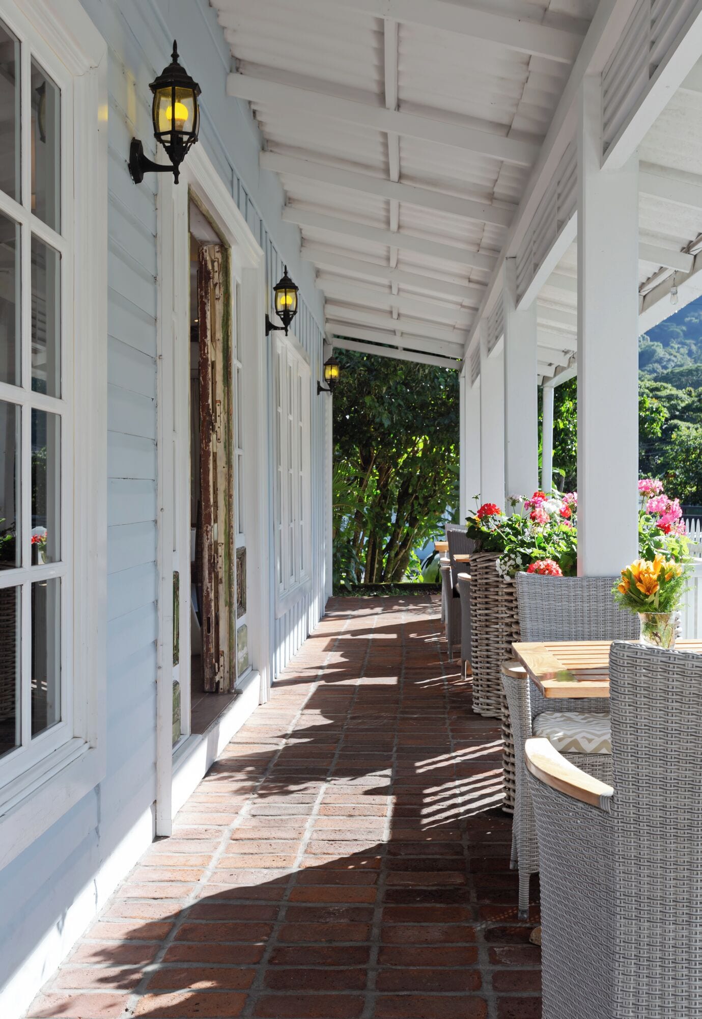 A covered outdoor area with wicker furniture and a brick floor.