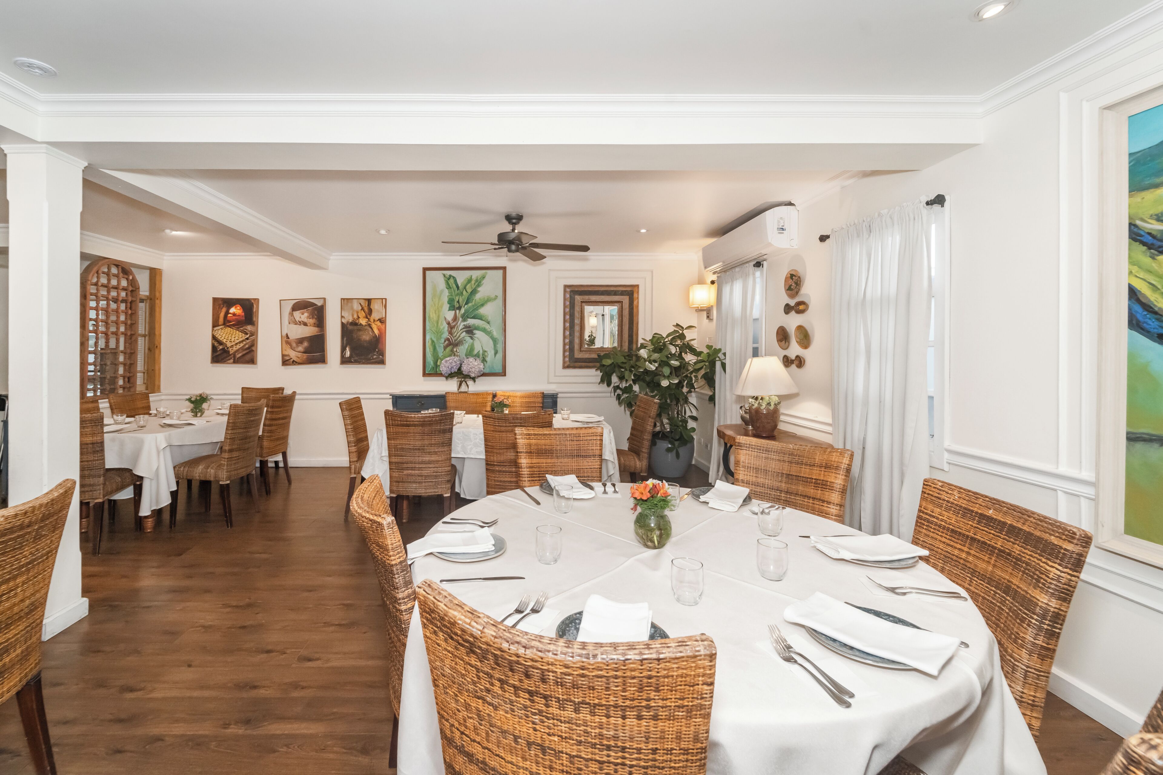 A dining area with round tables, wicker chairs, and a ceiling fan.