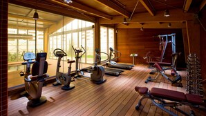 Un gimnasio con diverso equipamiento de ejercicio, amplias ventanas y suelo de madera.