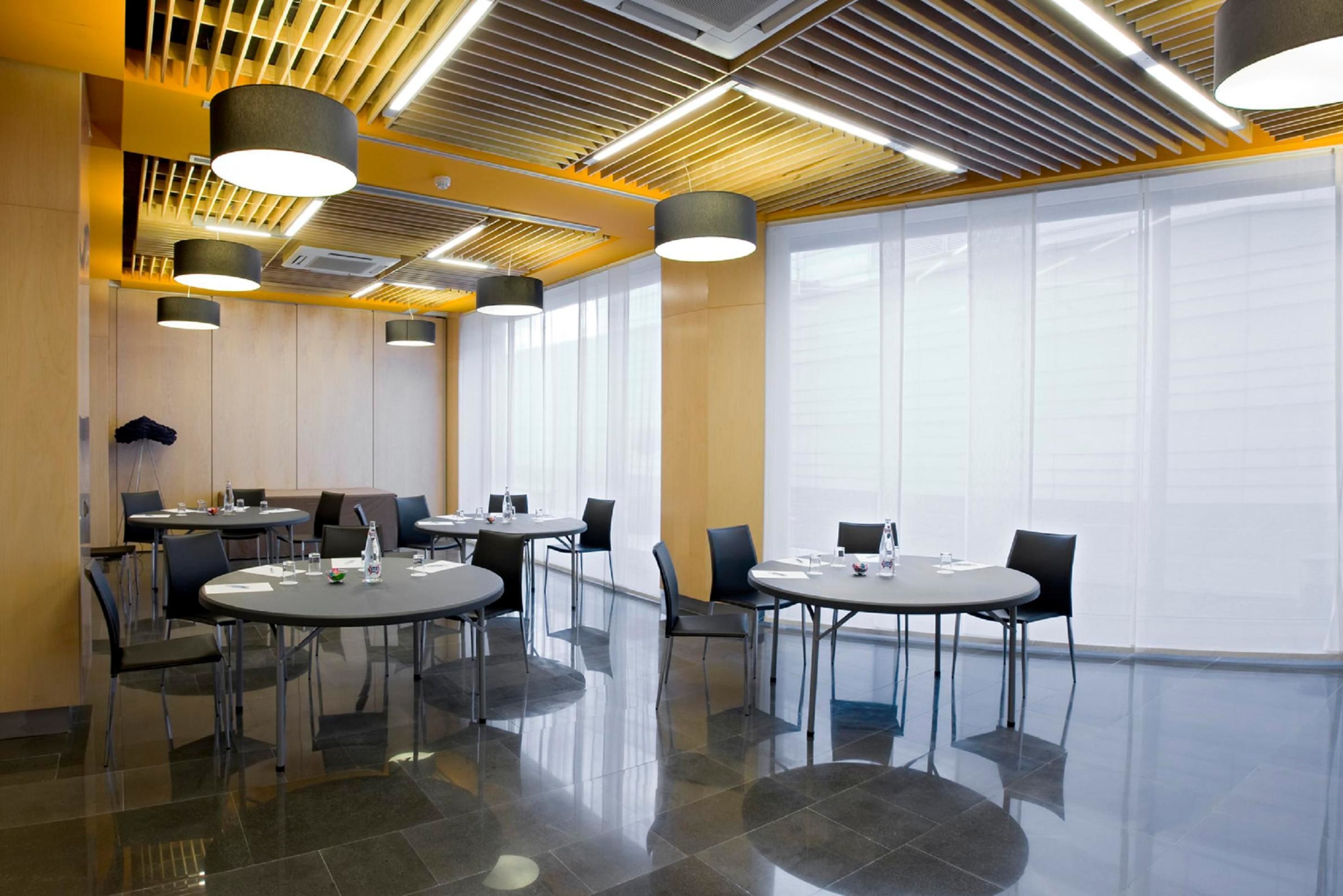 A modern conference room with round tables, chairs, and ceiling lights.