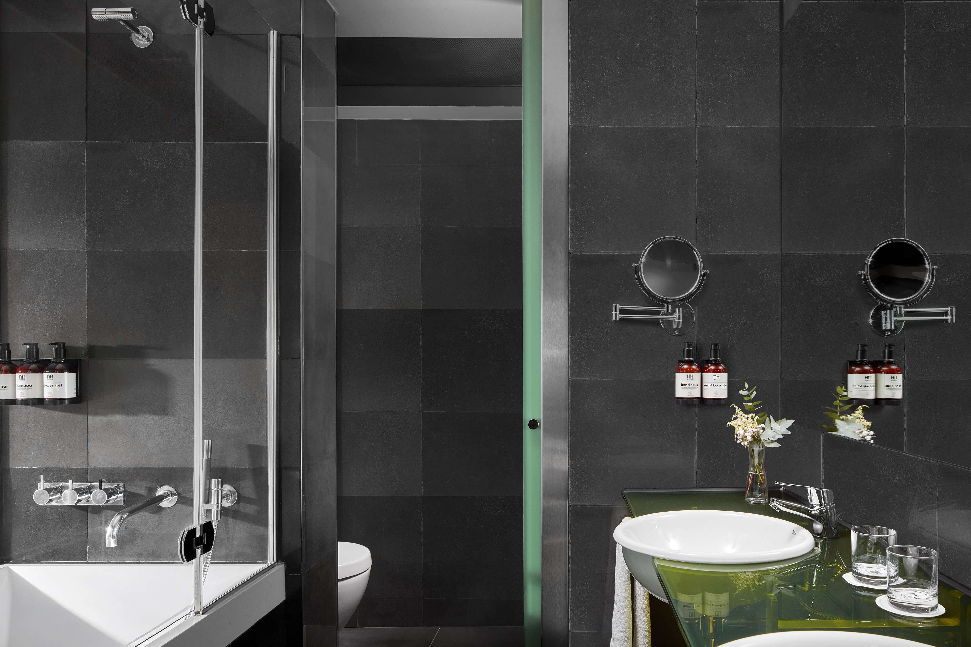 A modern bathroom with a glass-enclosed shower, a white sink with a green countertop, and two wall-mounted mirrors.