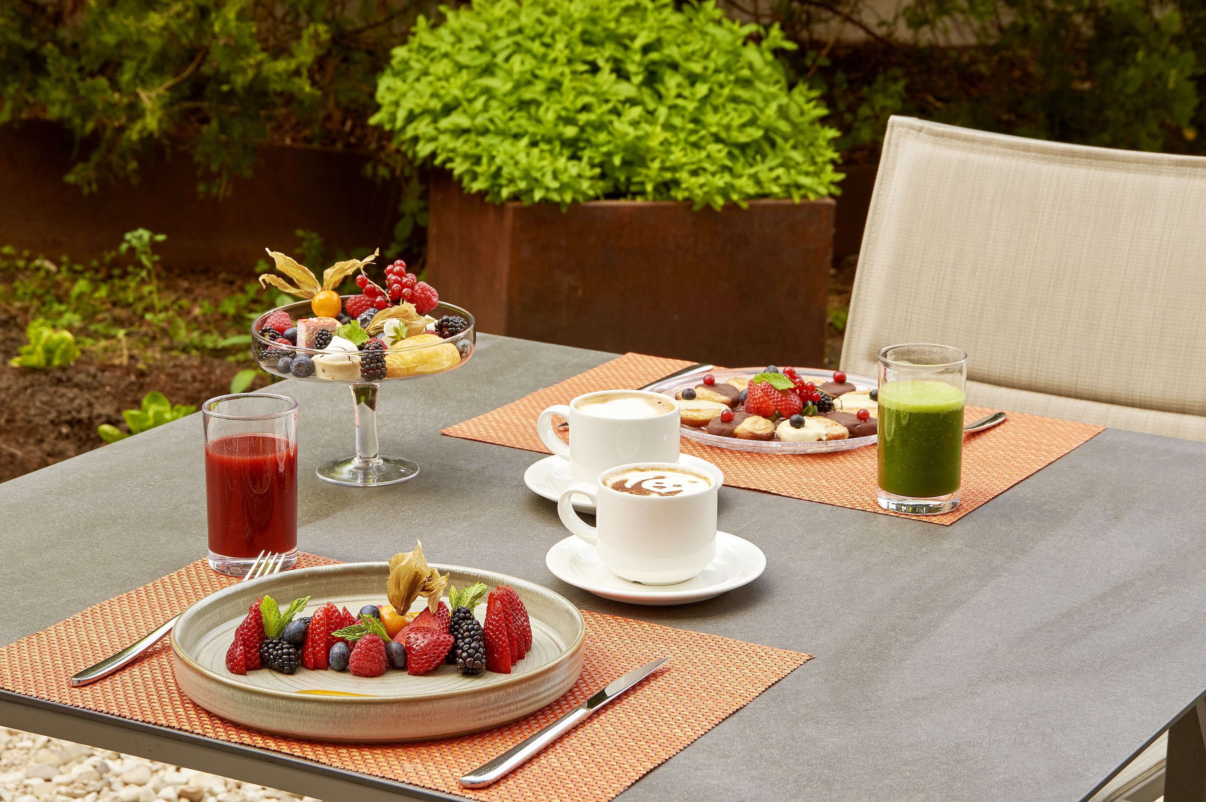 Una mesa dispuesta con un frutero, tazas de café y un batido verde.