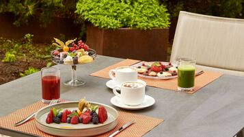 Una mesa dispuesta con un frutero, tazas de café y un batido verde.