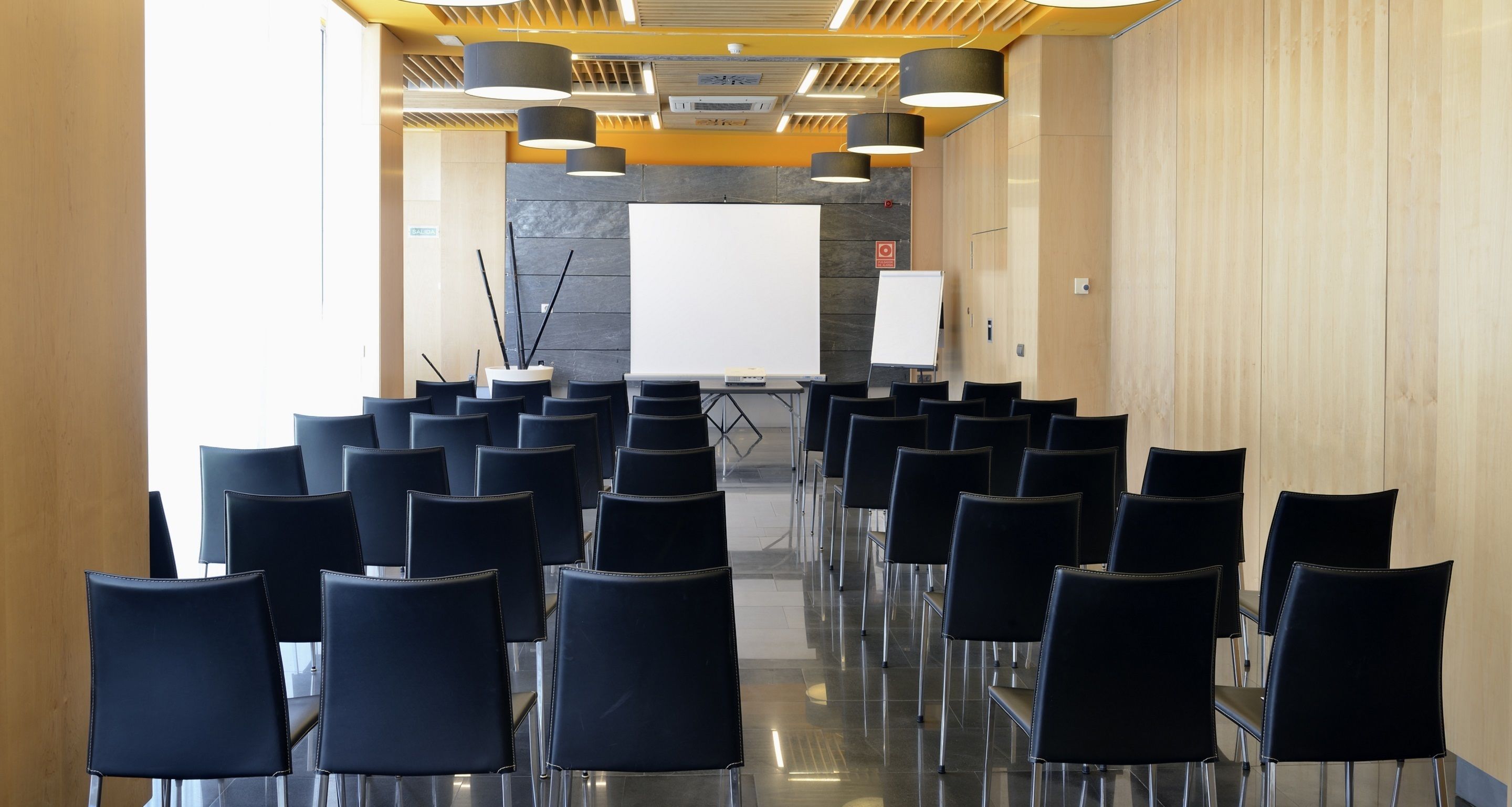 A conference room with rows of black chairs, a whiteboard, and a projector screen.