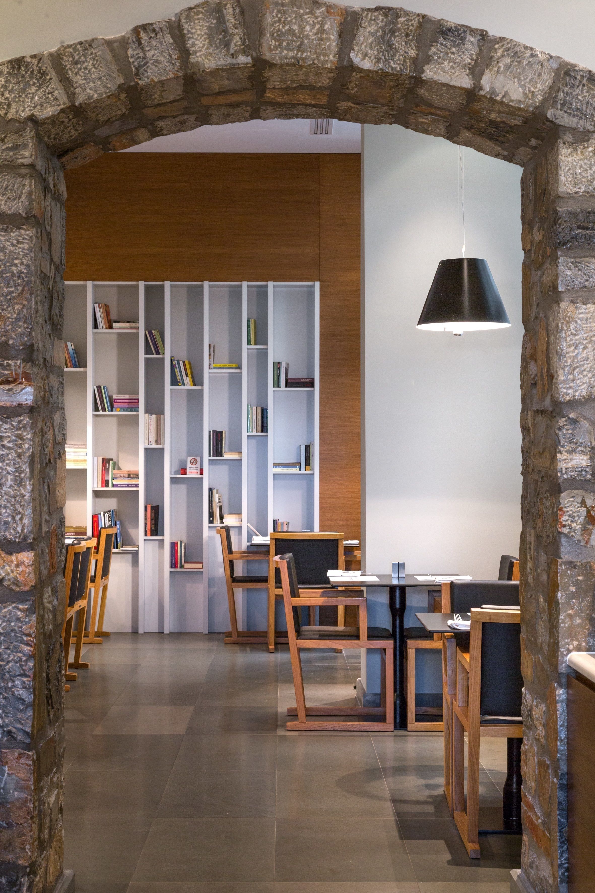 Una biblioteca con estanterías, mesas y sillas de madera, y un arco de piedra.