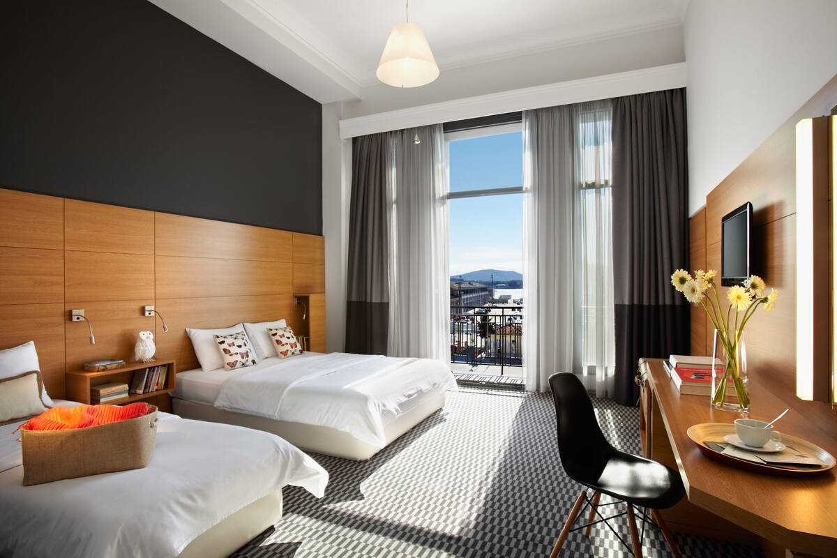 Habitación de hotel con dos camas, un escritorio con silla, televisión y vista a la ciudad.
