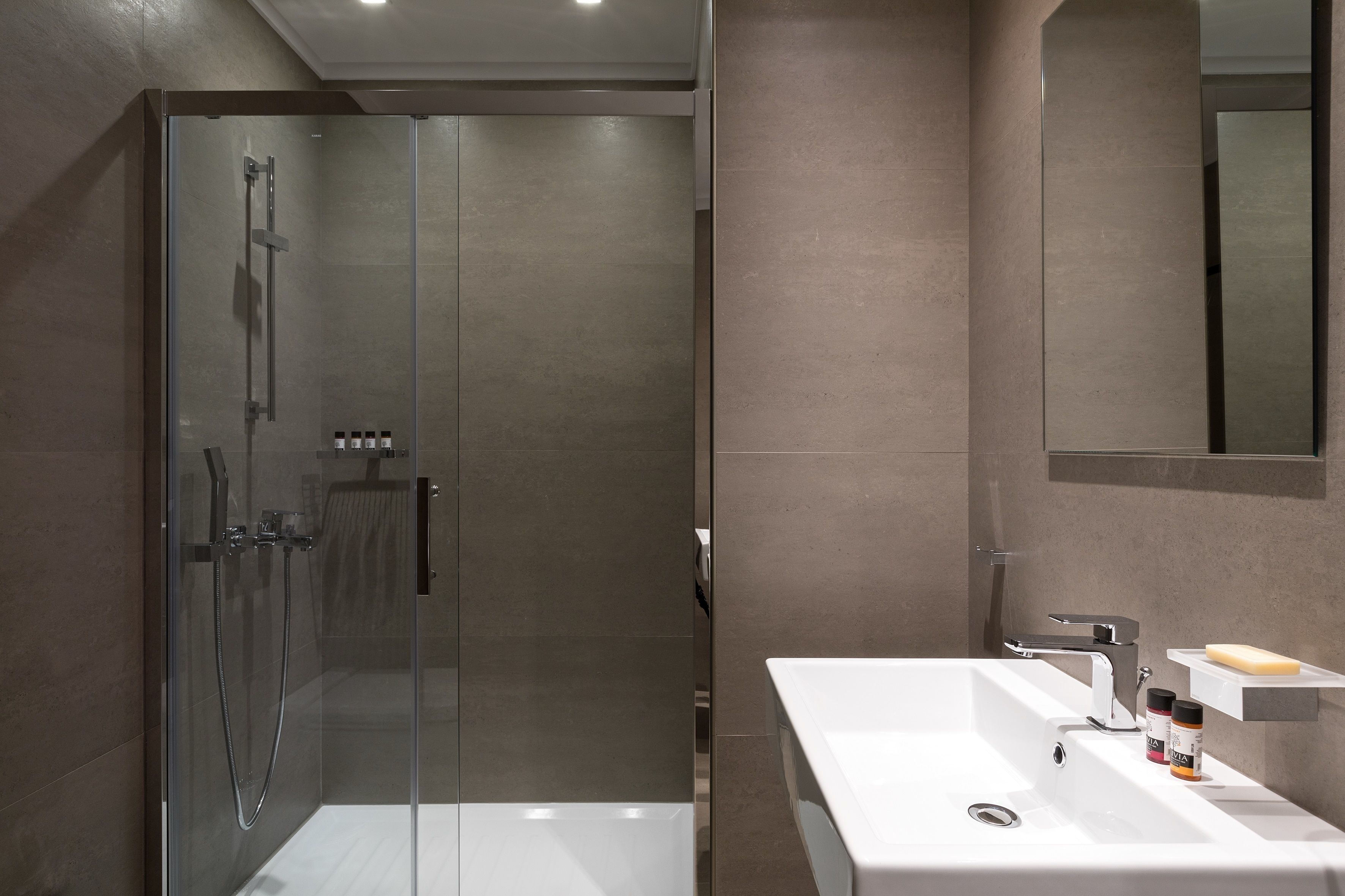 A modern bathroom with a glass-enclosed shower, a white sink with a mirror, and a shelf with toiletries.