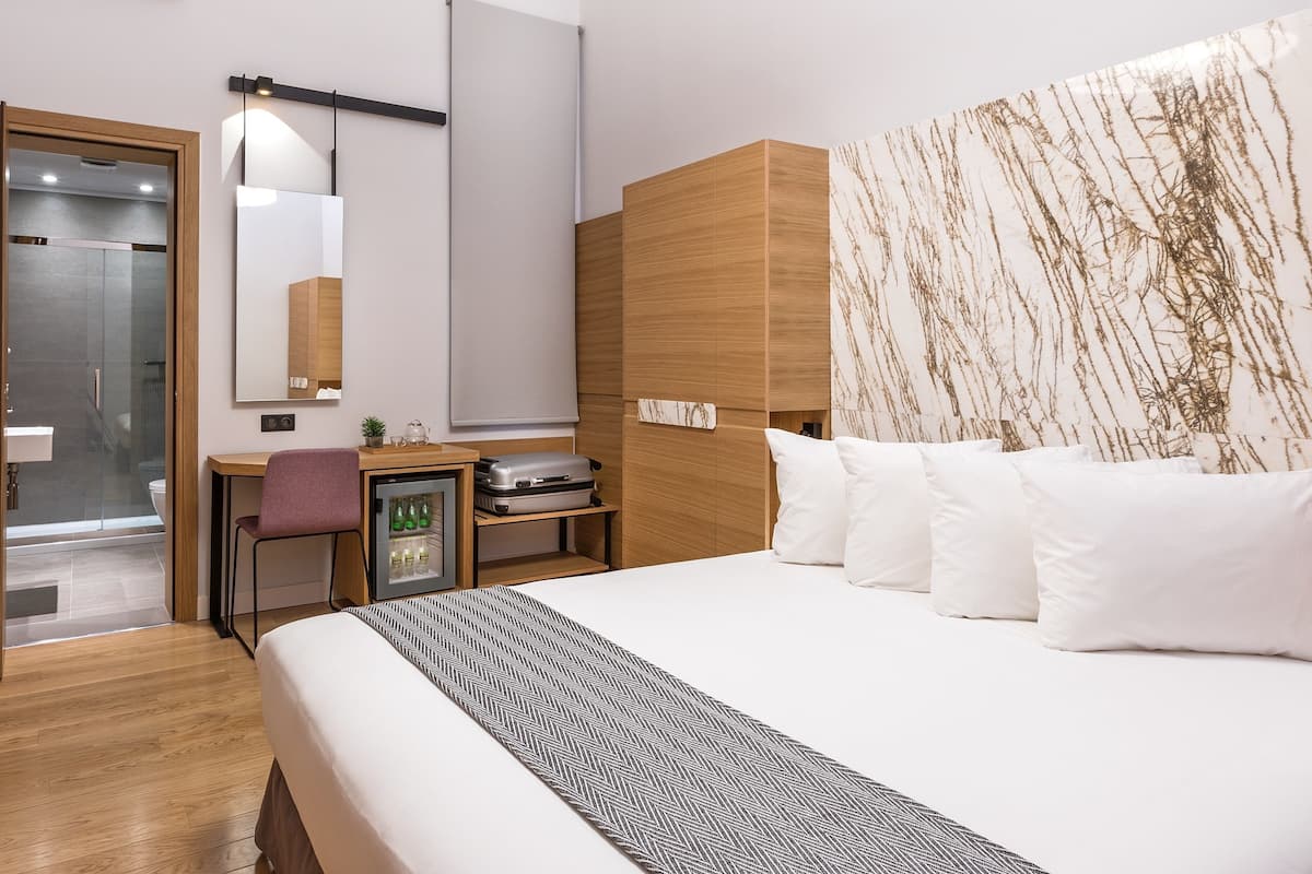 Habitación de hotel moderna con cama, escritorio, espejo, armario y zona de ducha.