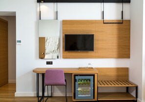 A modern room with a wooden desk, a purple chair, a built-in TV, and a mini-fridge with bottles.