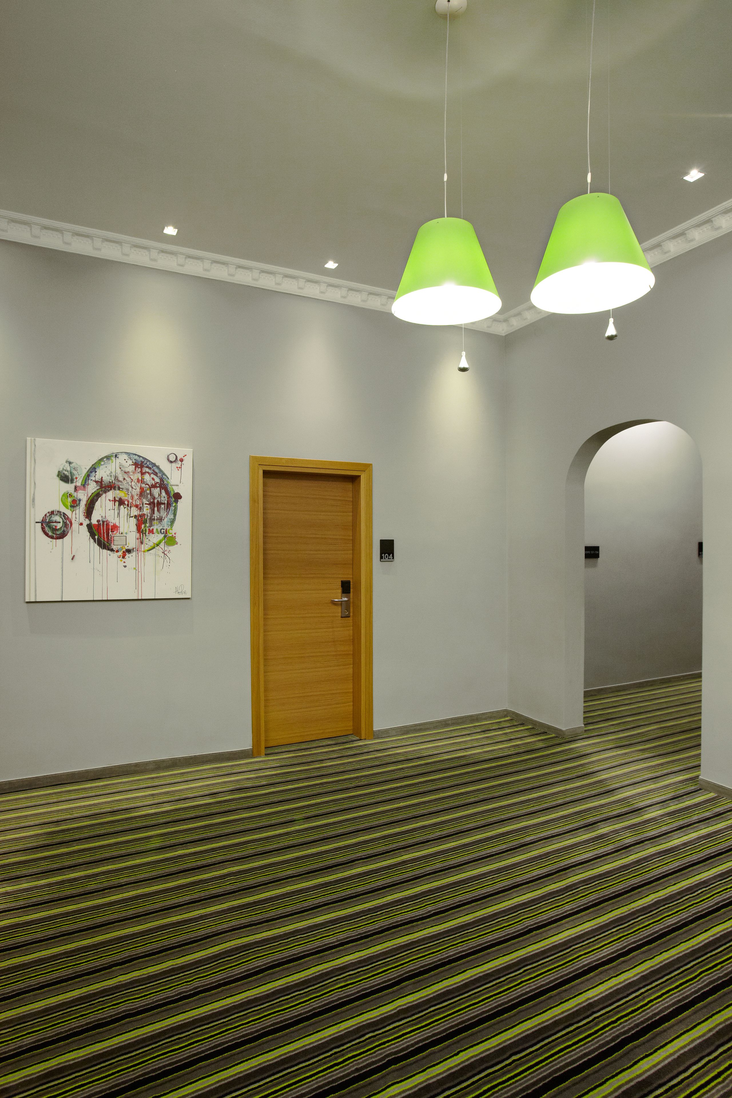 A hallway with a wooden door, green striped carpet, and a painting on the wall.