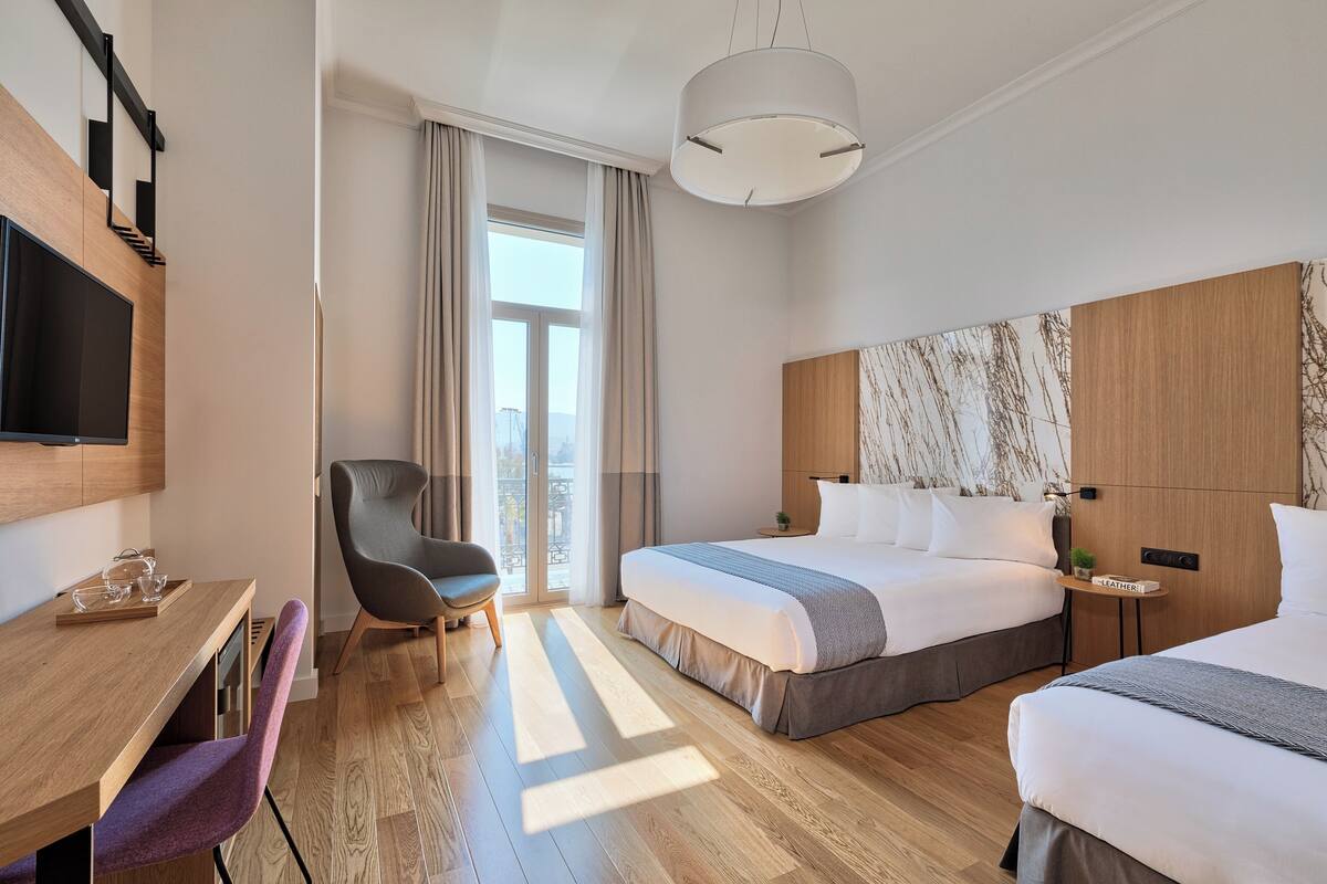 Habitación de hotel con una cama grande, un escritorio con silla, televisión y vistas al exterior.