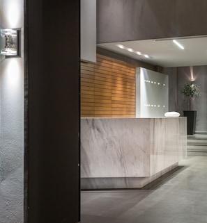 A modern reception desk with a wooden panel and marble top, a potted plant, and a security camera.