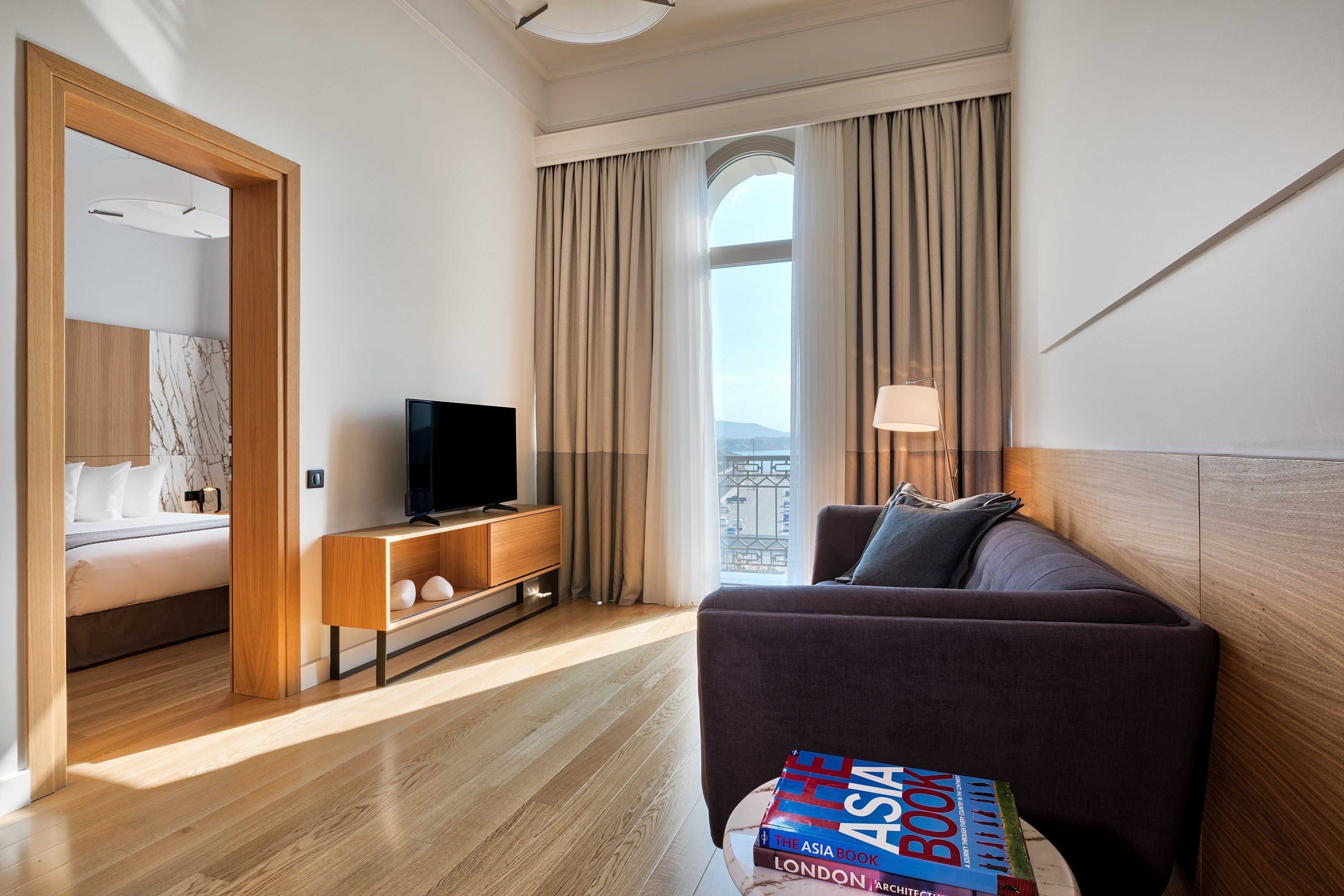 Habitación de hotel con cama, televisión, sofá, ventana con cortinas y vista a la ciudad.