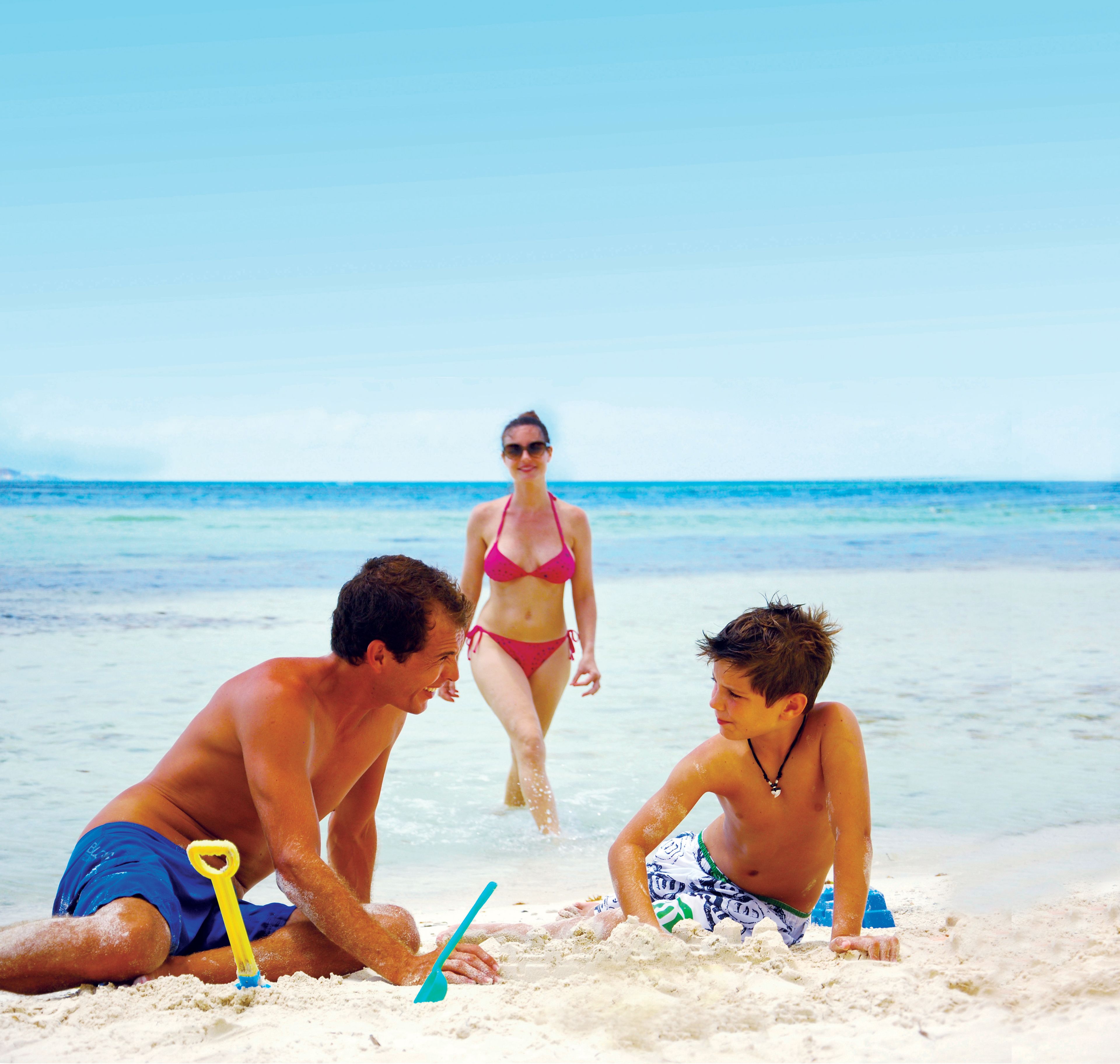 A beach scene with three people playing in the sand, a clear sky, and the ocean in the background.