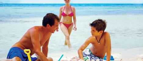 A beach scene with three people playing in the sand, a clear sky, and the ocean in the background.