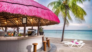 A beach bar with a thatched roof, white lounge chairs, and a palm tree. - Grand Oasis Palm - All Inclusive (Cancun)