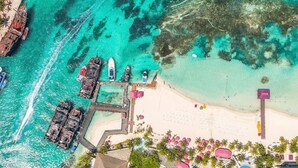 An aerial view of a beach resort with a dock, boats, and a sandy beach with umbrellas. - Grand Oasis Palm - All Inclusive (Cancun)