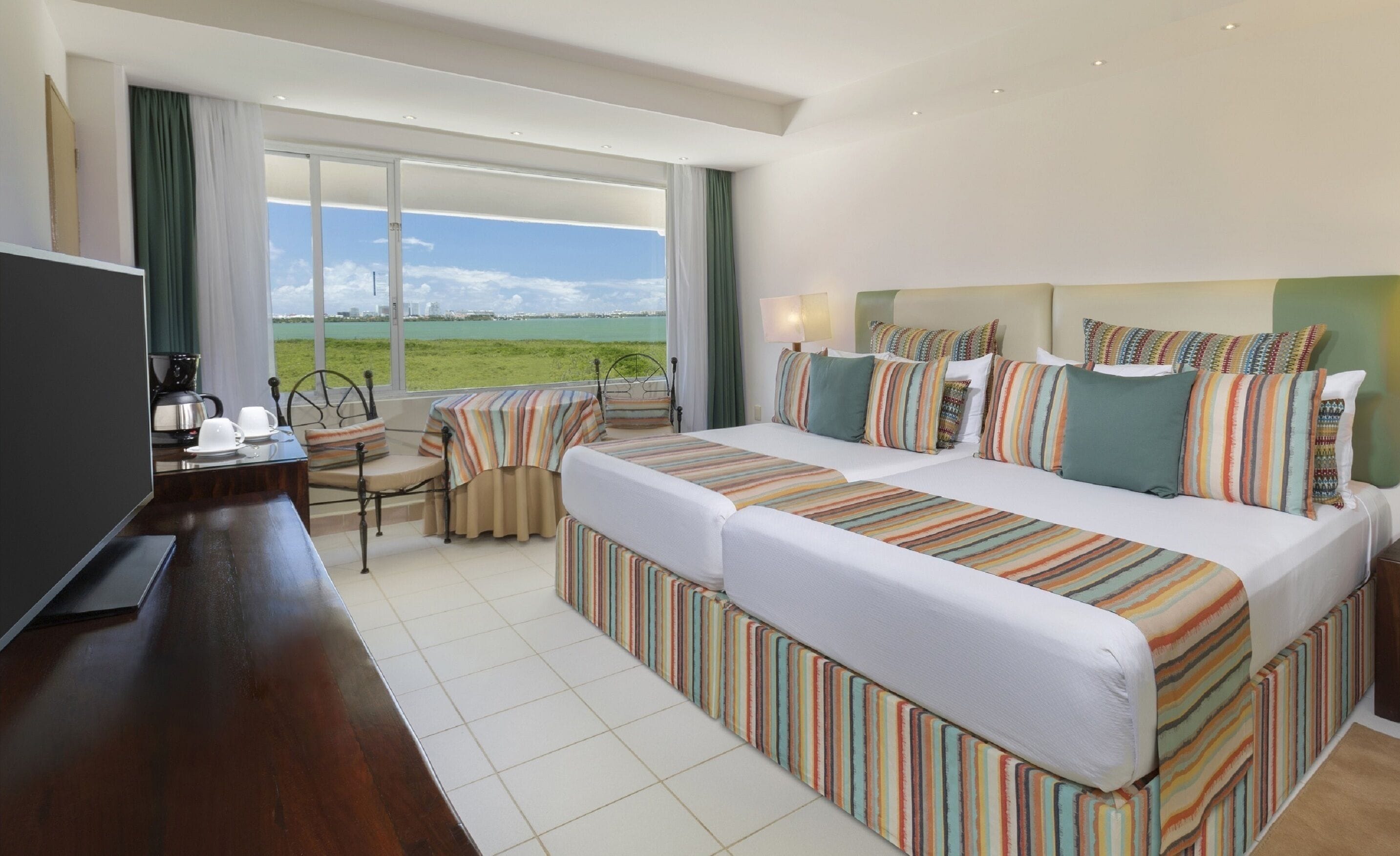 A hotel room with a large bed, a smaller bed, a desk with a chair, and a television.