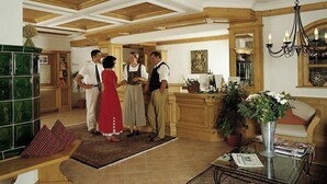 A spacious living area with a high ceiling, wooden beams, a green tiled fireplace, and a glass coffee table with magazines. - Hotel Ochsenwirtshof (Bad Rippoldsau-Schapbach)