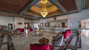 A spacious lobby with a grand chandelier, red and white chairs, and intricate ceiling designs. - Mogador Kasbah (Marrakech)