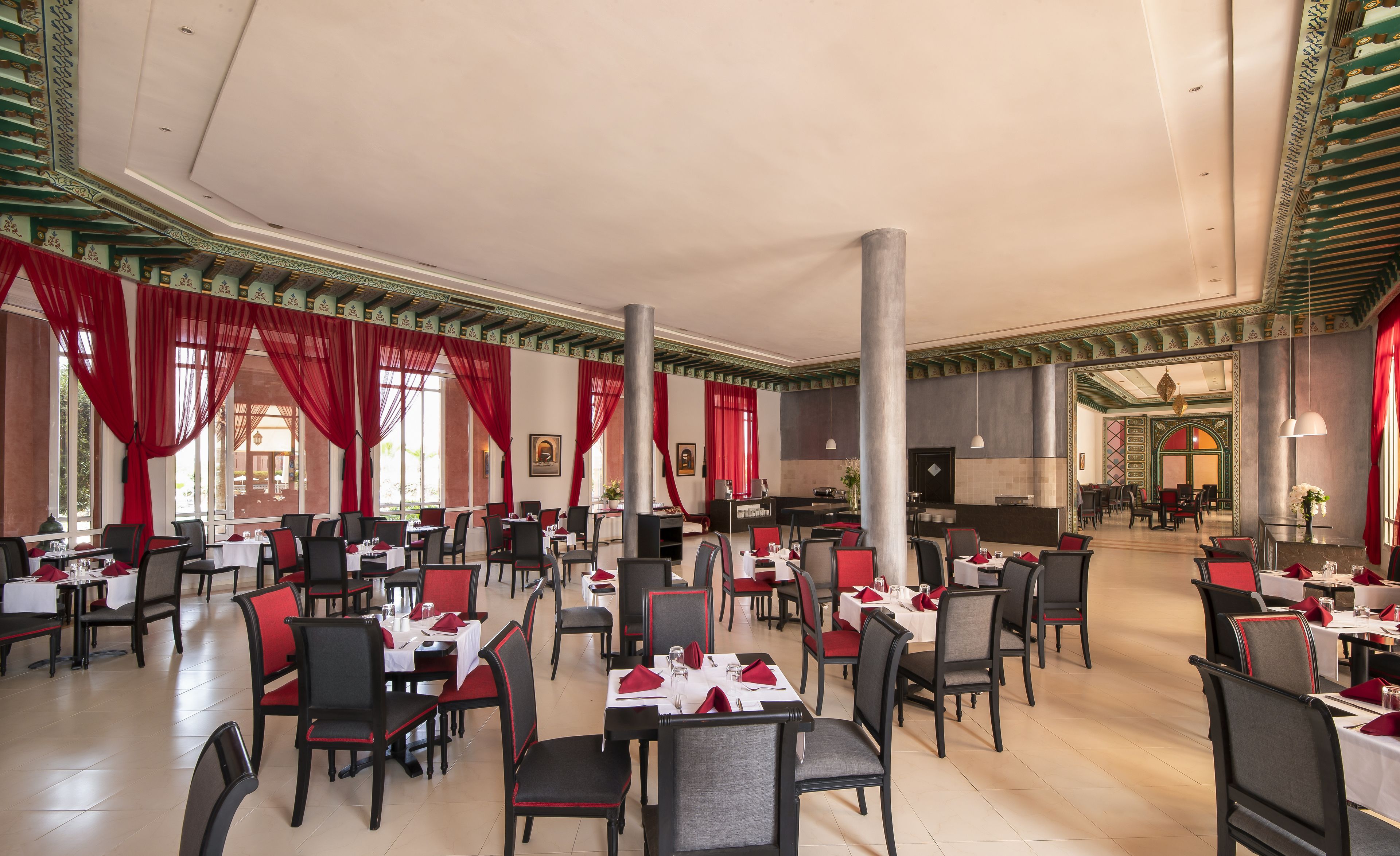A spacious restaurant with high ceilings, red drapes, and traditional decor. Tables are neatly arranged with white tablecloths and red napkins.