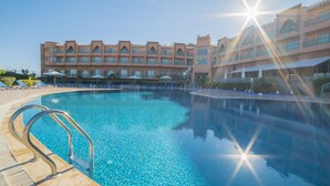 A swimming pool with clear blue water, surrounded by lounge chairs and umbrellas, with a hotel building in the background. - Mogador Kasbah (Marrakech)