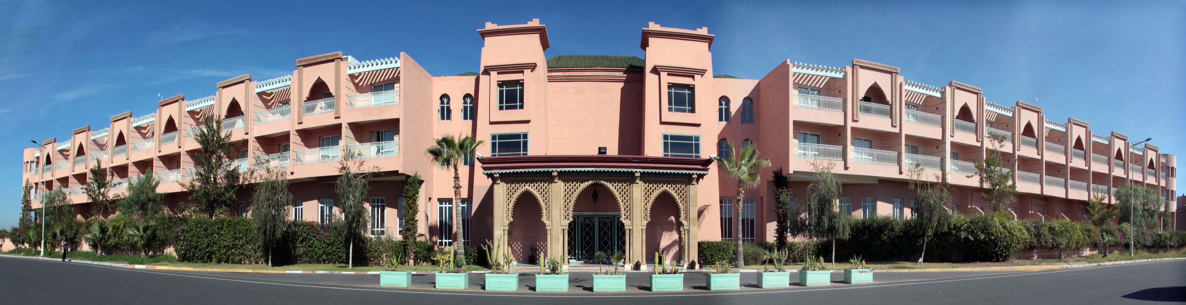 Un hôtel rose à plusieurs étages, doté de balcons et d’une entrée centrale ornée d’arcs décoratifs.