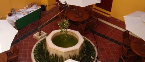 A courtyard with a fountain, outdoor seating, and a table with items on it.