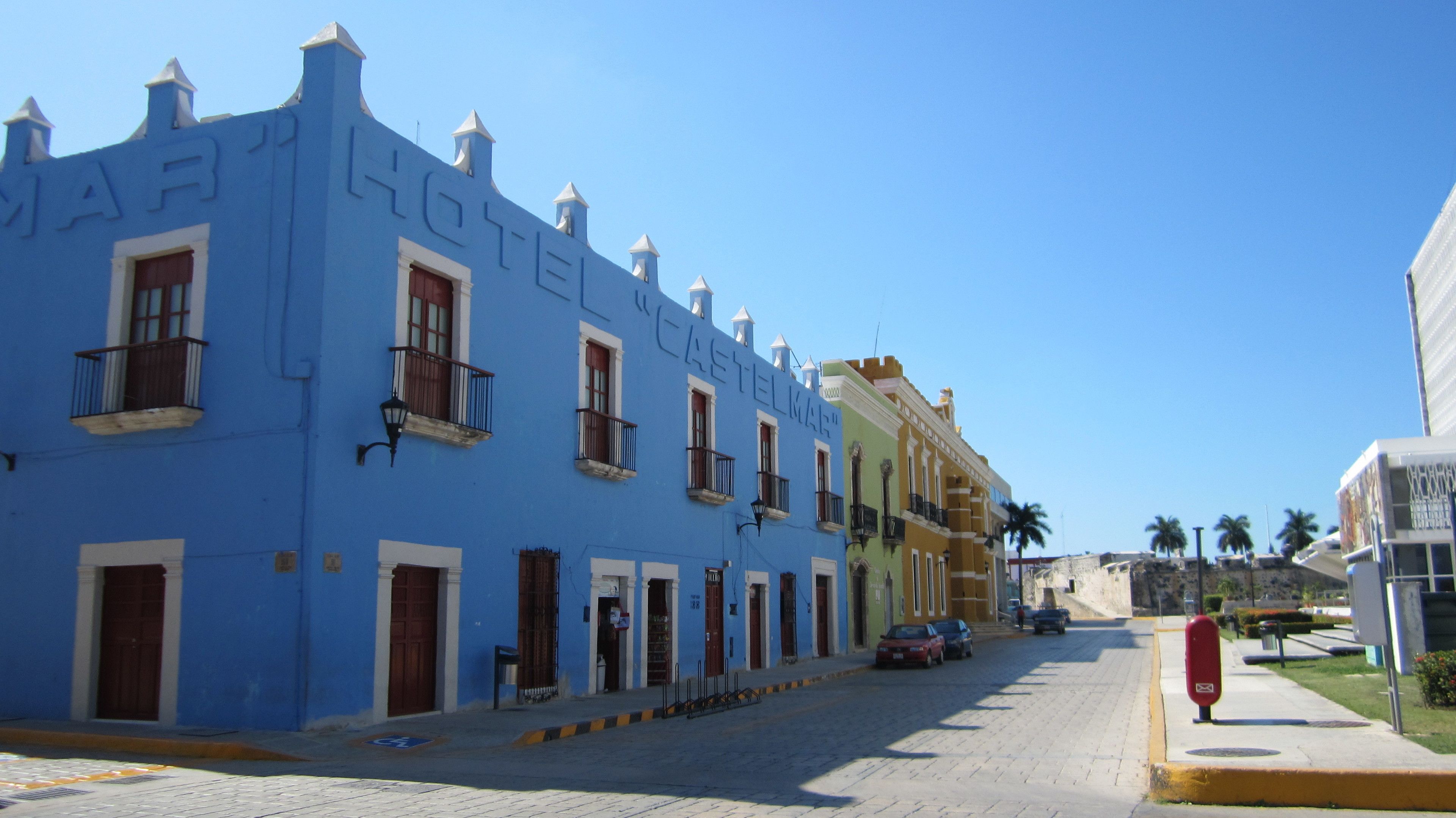 A row of colorful buildings with balconies, a clear blue sky, and a paved street.