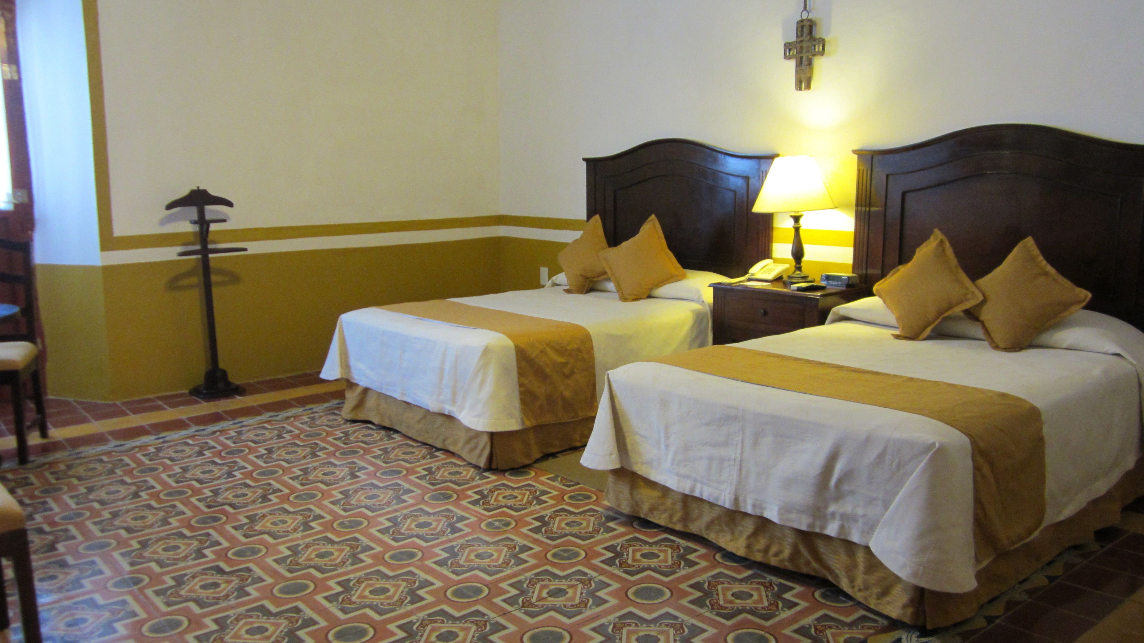 A hotel room with two beds, a patterned floor, and a nightstand with a lamp.