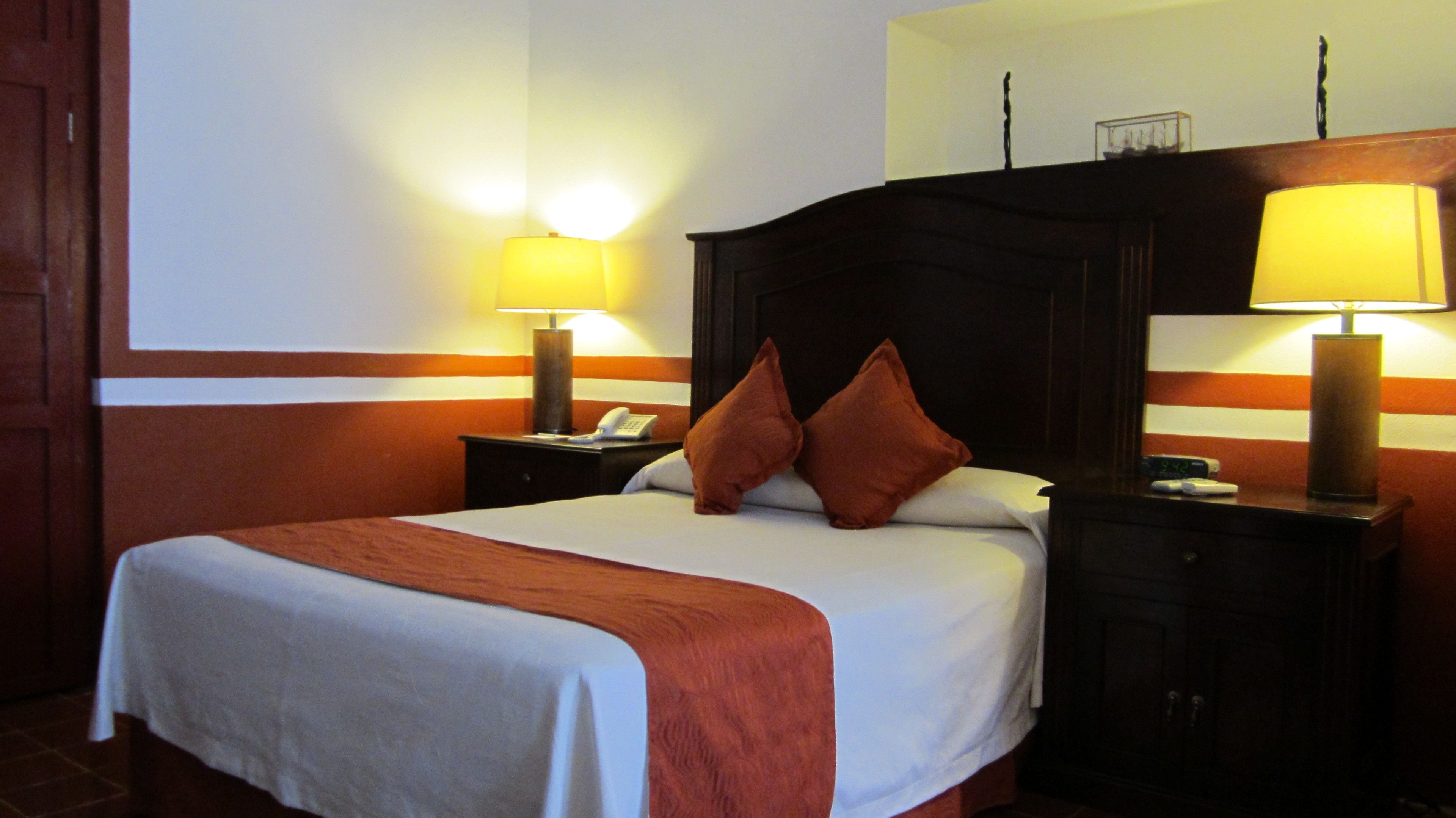 A hotel room with a large bed, two bedside lamps, a telephone, and a nightstand.
