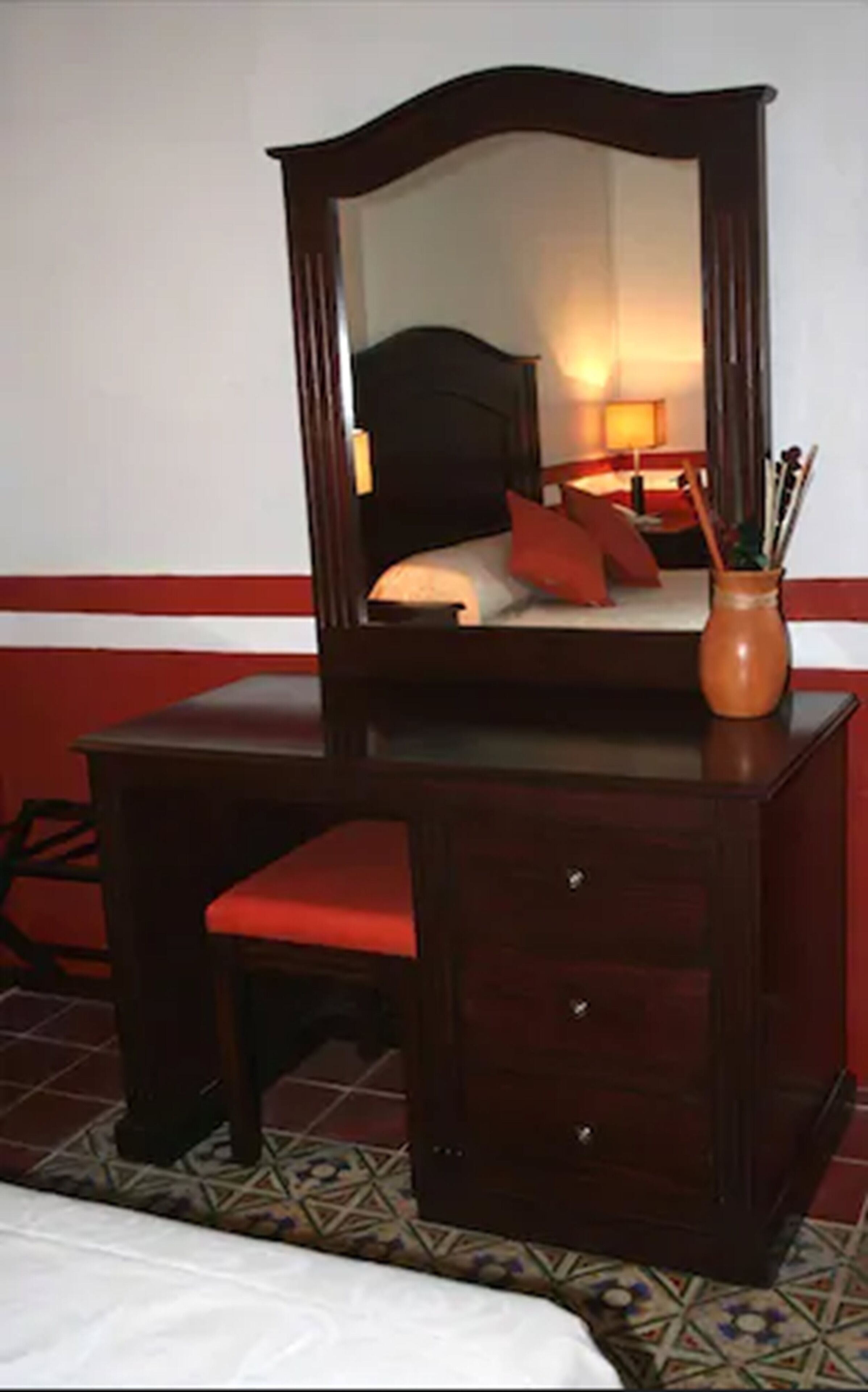A wooden dresser with a mirror, a red chair, and a vase with pens.