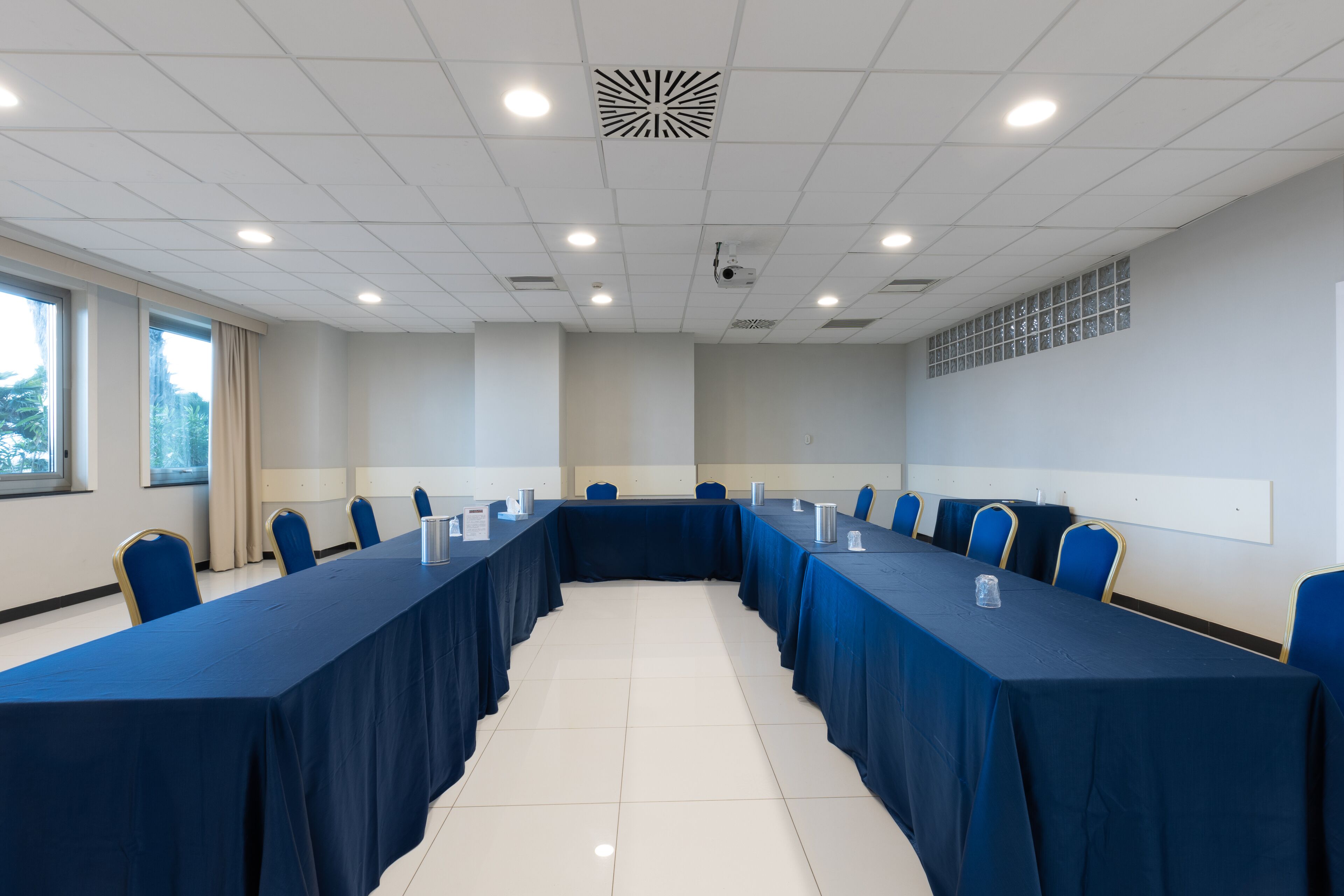 Un salón de conferencias con una mesa larga, sillas azules y un proyector en el techo.