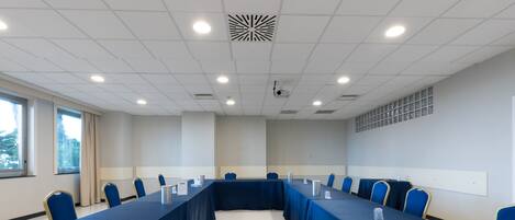 Un salón de conferencias con una mesa larga, sillas azules y un proyector en el techo.
