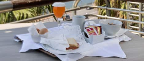 A breakfast setup with eggs, toast, and a drink on a table overlooking a scenic view of the sea and mountains.