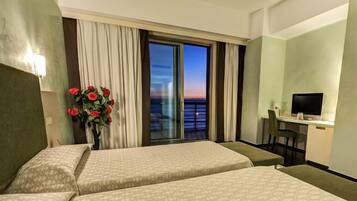 Habitación de hotel con dos camas, un escritorio con silla, televisión y vista al atardecer por la ventana.