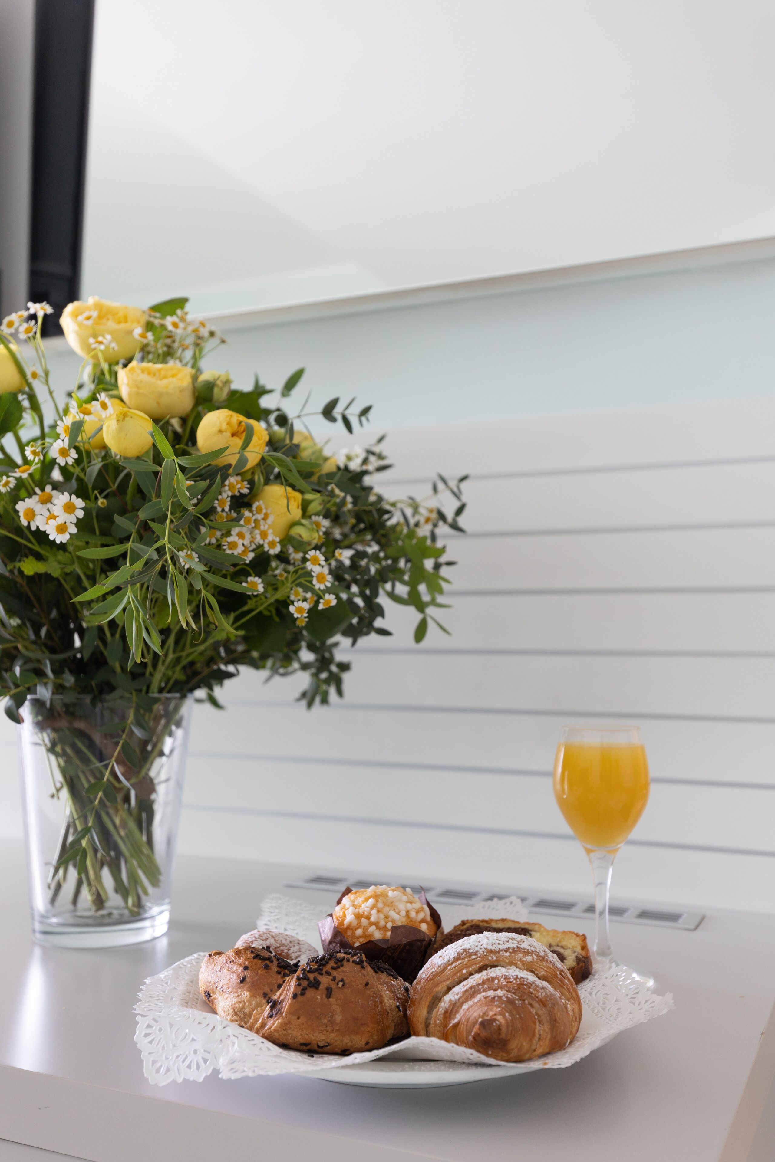 A table with pastries, a glass of orange juice, and a bouquet of yellow flowers.