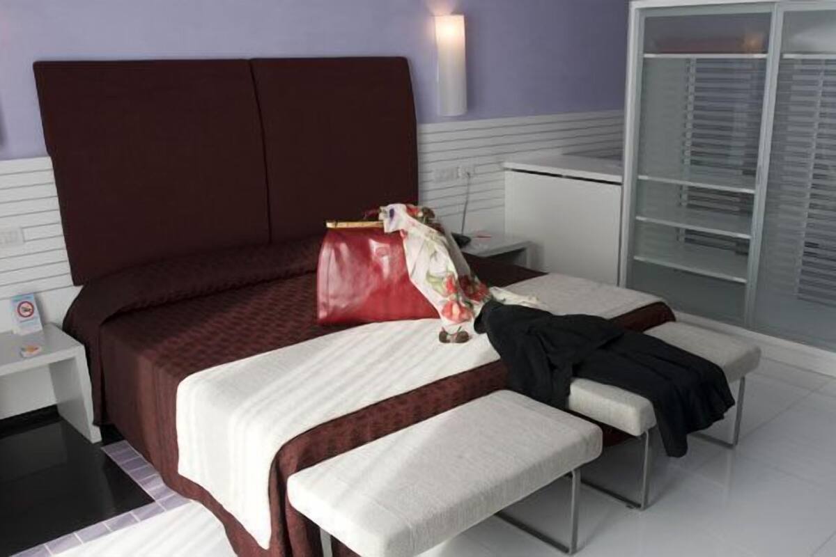 Una habitación de hotel moderna con una cama grande, una mesita de noche, un banco y un armario.