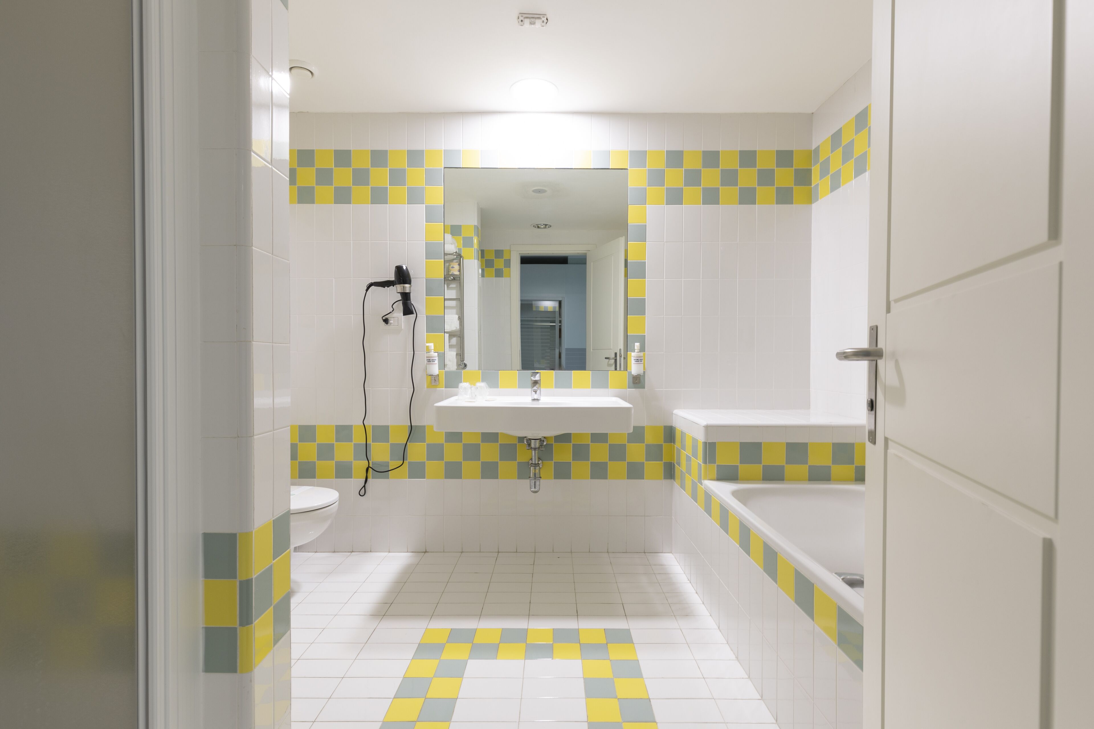 Baño con lavamanos, inodoro y bañera, con un diseño de baldosas a cuadros.
