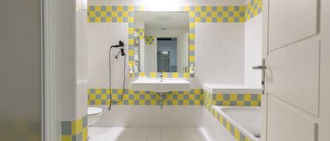 Baño con lavamanos, inodoro y bañera, con un diseño de baldosas a cuadros.