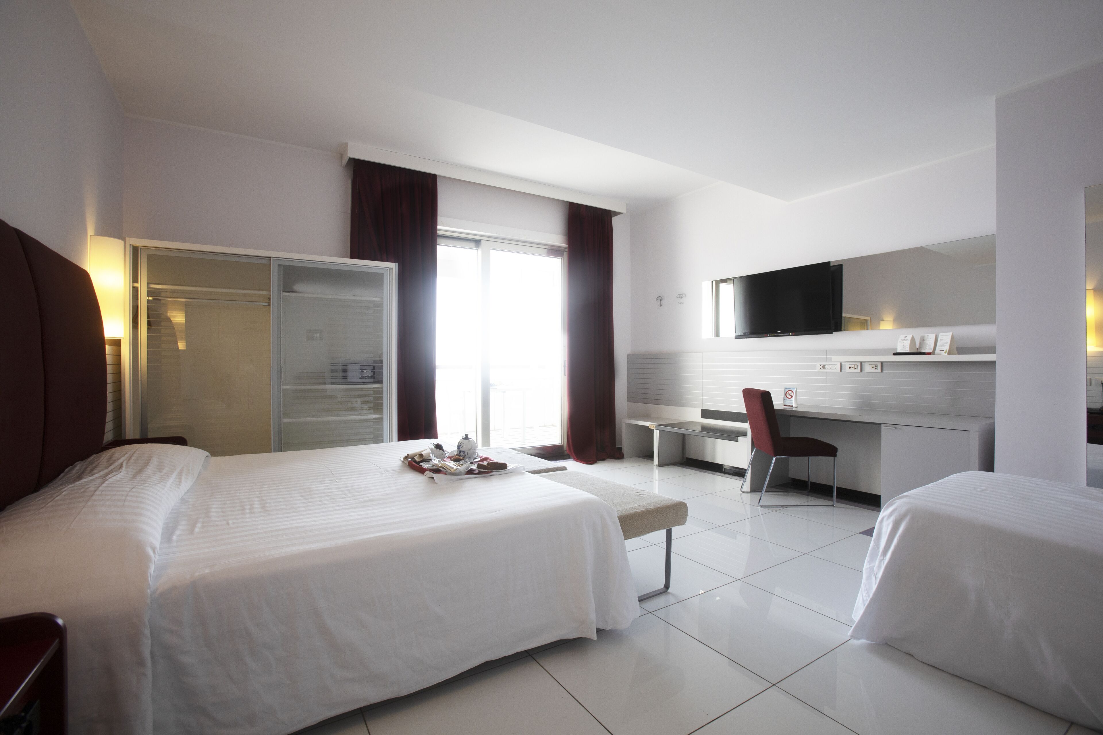 A hotel room with two beds, a desk, a chair, a wardrobe, and a TV.